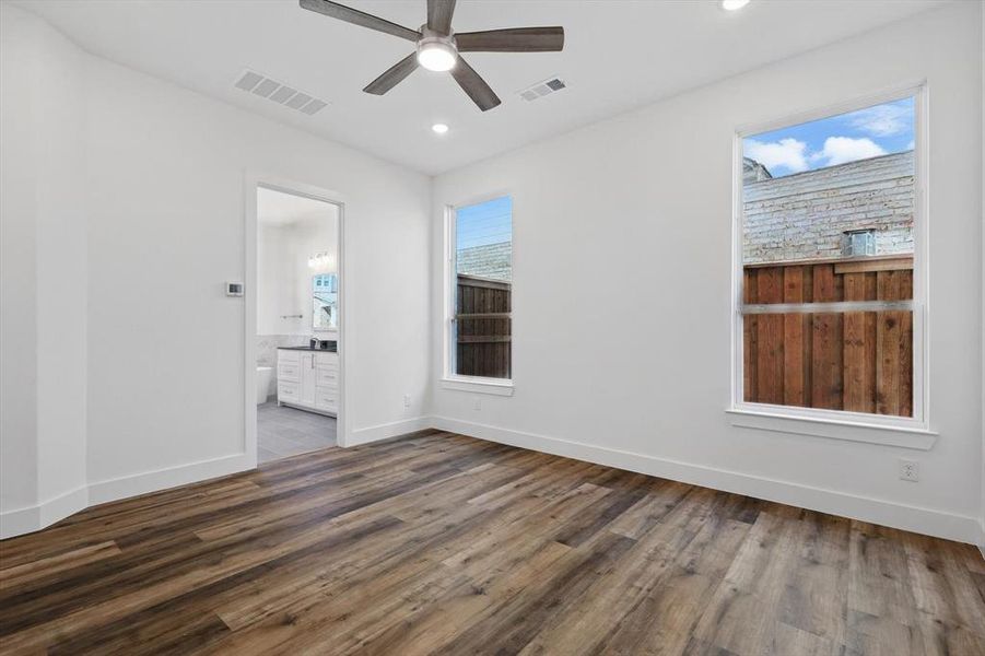 Empty room featuring dark wood-type flooring, visible vents, baseboards, and a ceiling fan