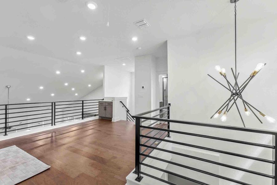 Expansive loft area featuring wood-finish flooring, a contemporary chandelier, recessed lighting, and black horizontal bar railings