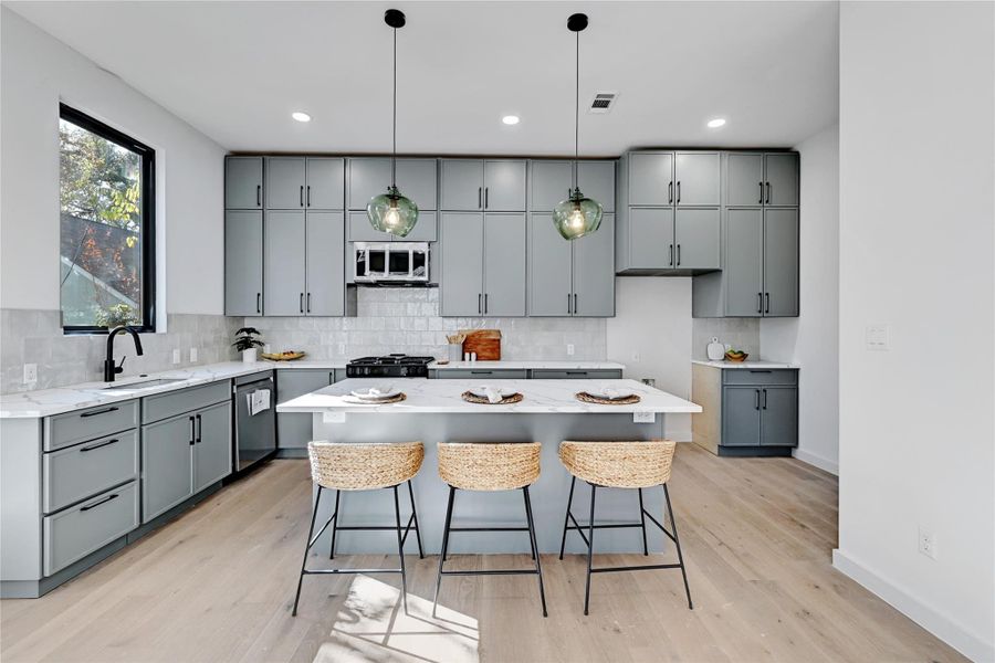 Kitchen featuring a sink, white microwave, stainless steel dishwasher, and gray cabinetry