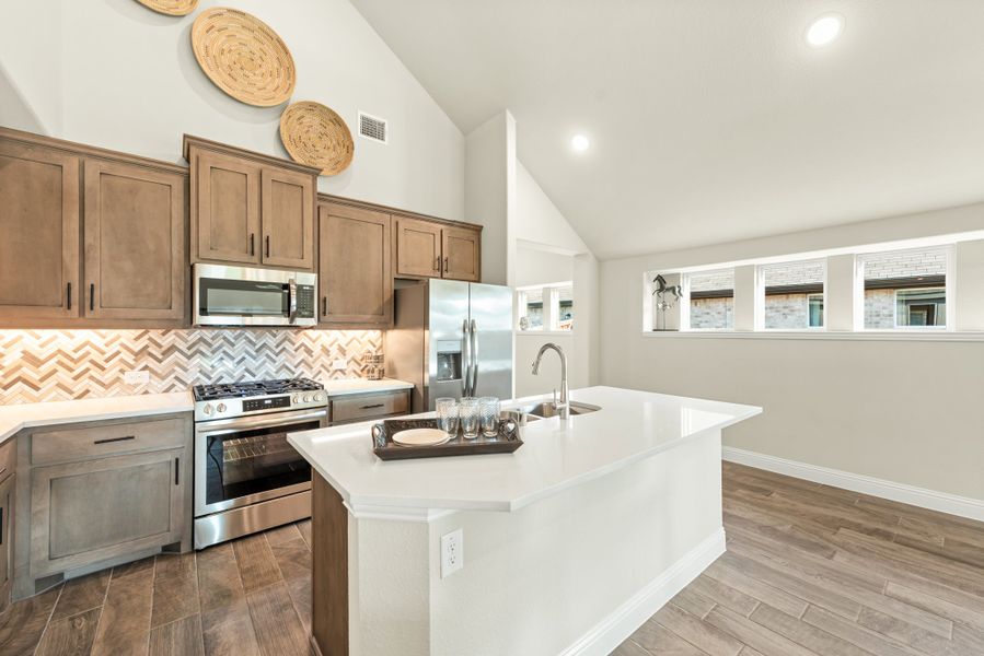 Kitchen with white island, stainless steel appliances, wood cabinets, and vaulted ceiling