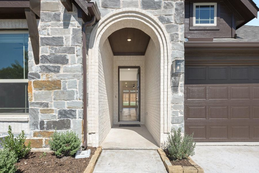 Home entrance with arched brick entryway, stone exterior, and brown two-car garage door