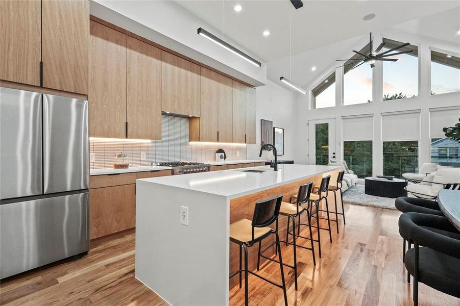 Kitchen featuring high vaulted ceiling, stainless steel refrigerator, an island with sink, ceiling fan, and decorative backsplash