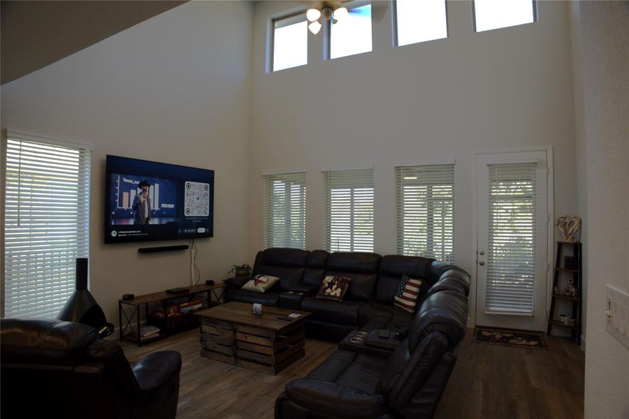 Living room featuring a high ceiling, healthy amount of natural light, dark wood-type flooring, and a ceiling fan Living room featuring a high ceiling, healthy amount of natural light, dark wood-type flooring, and a ceiling fan