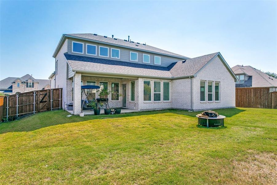 Back of house featuring roof with shingles, a fenced backyard, a fire pit, a patio, and brick siding