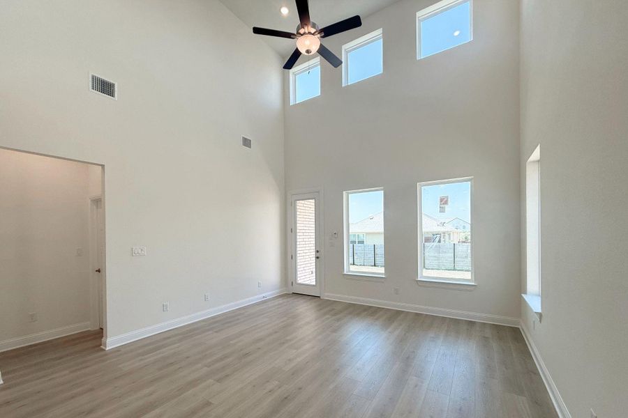 Two-story living area featuring a vaulted ceiling with a contemporary ceiling fan, multiple windows including transom lites, wood-finish flooring, and a glass-paneled exterior door Two-story living area featuring a vaulted ceiling with a contemporary ceiling fan, multiple windows including transom lites, wood-finish flooring, and a glass-paneled exterior door