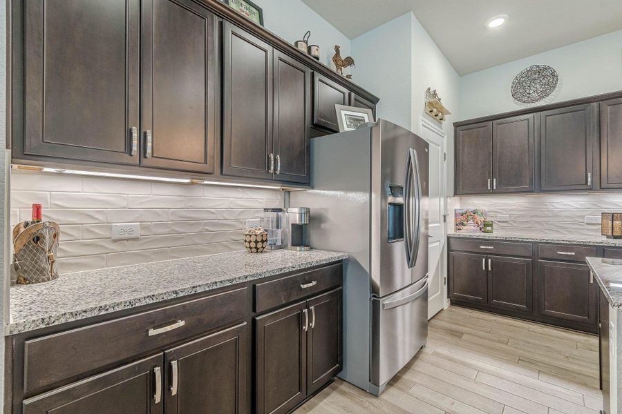 Kitchen featuring stainless steel fridge, tasteful backsplash, dark brown cabinetry, and light wood finished floors
