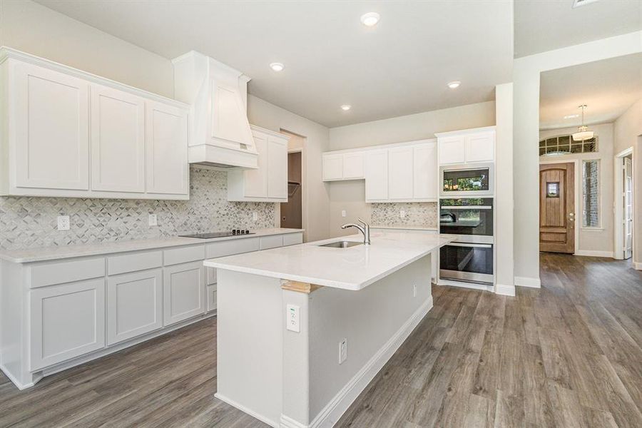 Kitchen with white cabinets, stainless steel double oven, backsplash, dark wood-style flooring, and light stone counters Kitchen with white cabinets, stainless steel double oven, backsplash, dark wood-style flooring, and light stone counters