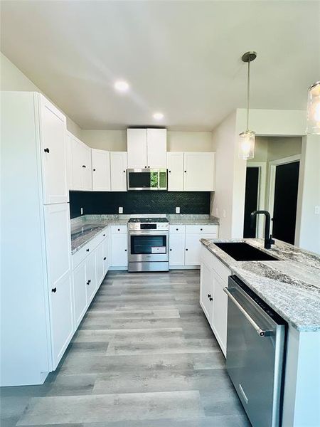 Kitchen featuring appliances with stainless steel finishes, light hardwood / wood-style flooring, sink, hanging light fixtures, and light stone countertops