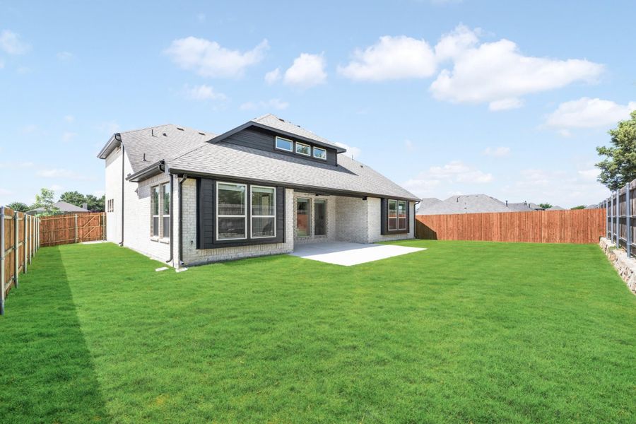 Backyard of a brick home with dark trim, concrete patio, green lawn, and wood privacy fence