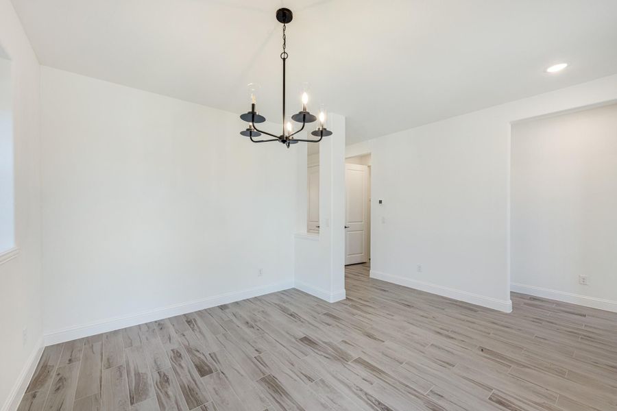 Empty dining room with black chandelier, white walls, and light wood-look tile floors Empty dining room with black chandelier, white walls, and light wood-look tile floors