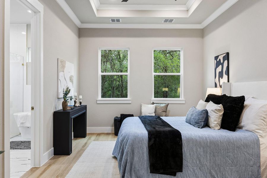 A tranquil primary bedroom features hardwood flooring and a stylish tray ceiling.