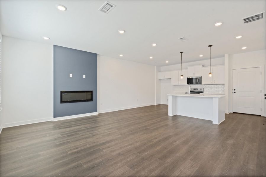 Open-concept living space featuring wood-finish flooring, recessed lighting, and a linear fireplace with an accent wall