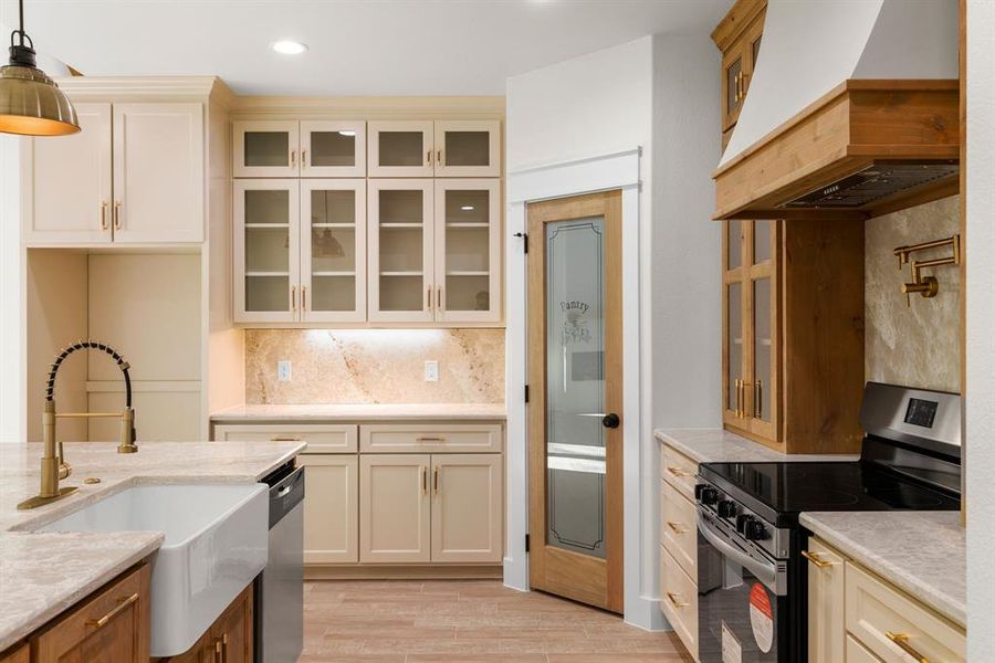 Kitchen with premium range hood, hanging light fixtures, sink, light hardwood / wood-style flooring, and appliances with stainless steel finishes