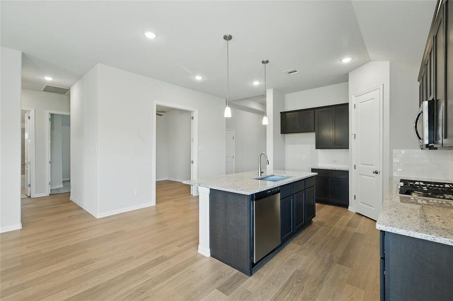 Kitchen with a sink, stainless steel appliances, light wood-style floors, backsplash, and light stone counters