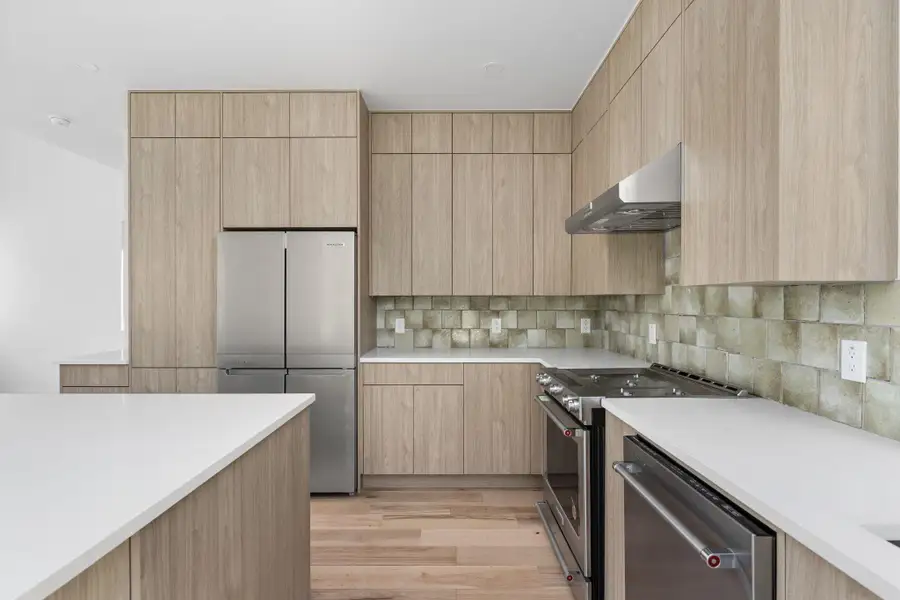 Kitchen featuring stainless steel appliances, light brown cabinets, and exhaust hood