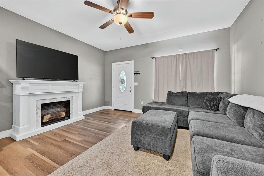 Living room with ceiling fan, wood finished floors, and a premium fireplace Living room with ceiling fan, wood finished floors, and a premium fireplace