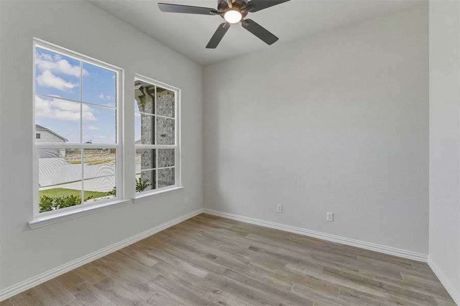 Room featuring two large windows with grid muntins, wood-finish flooring, a ceiling fan with integrated lighting, and neutral wall paint Room featuring two large windows with grid muntins, wood-finish flooring, a ceiling fan with integrated lighting, and neutral wall paint