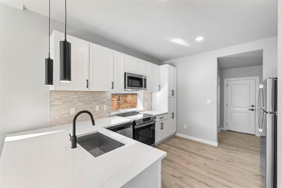 Kitchen with stainless steel appliances, white cabinets, light stone counters, decorative backsplash, and light wood finished floors
