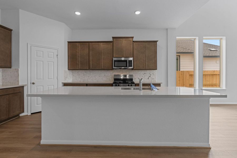 This light and bright kitchen features a large quartz island, dark stained cabinets, a large sink overlooking your family room, recessed lighting, and beautiful backsplash. This light and bright kitchen features a large quartz island, dark stained cabinets, a large sink overlooking your family room, recessed lighting, and beautiful backsplash.