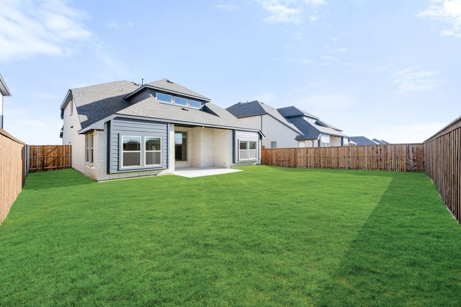 Rear view of two-story home with covered patio, large grassy backyard, and wood privacy fence Rear view of two-story home with covered patio, large grassy backyard, and wood privacy fence