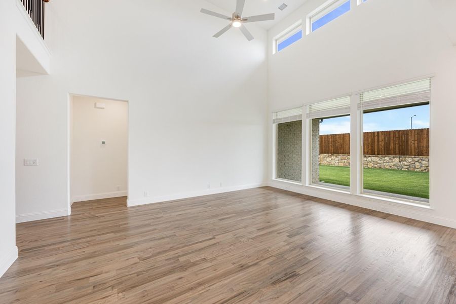 Open living room with two-story ceiling, ceiling fan, hardwood floors, and large windows overlooking backyard Open living room with two-story ceiling, ceiling fan, hardwood floors, and large windows overlooking backyard