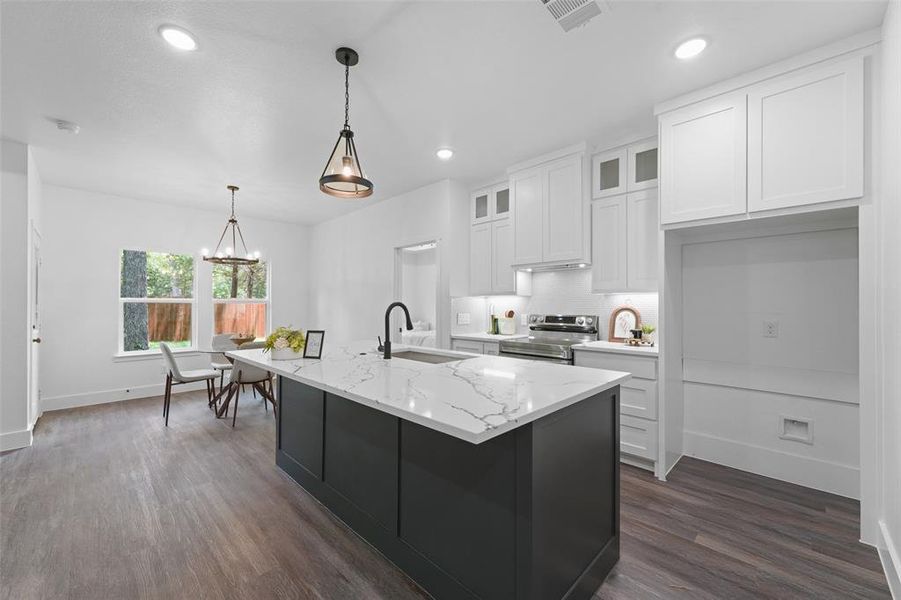 Kitchen featuring an expansive island with a stone countertop, dark cabinetry, and integrated sink Kitchen featuring an expansive island with a stone countertop, dark cabinetry, and integrated sink