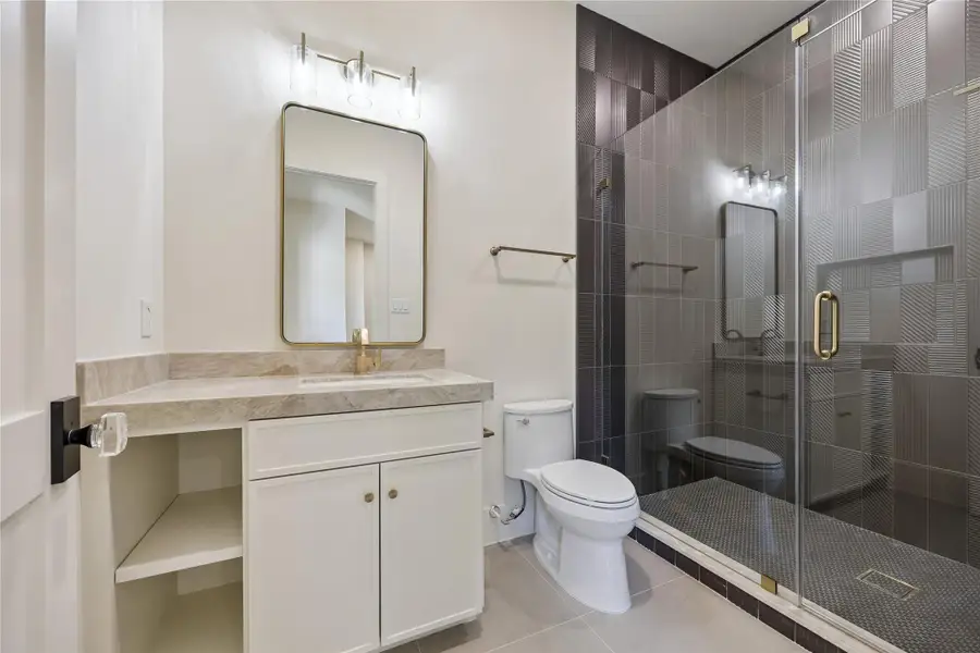 SECONDARY BATH II: Sleek secondary bath showcases a walk-in glass-enclosed shower, designer porcelain surround, and Mont Blanc Gold Quartzite countertop.