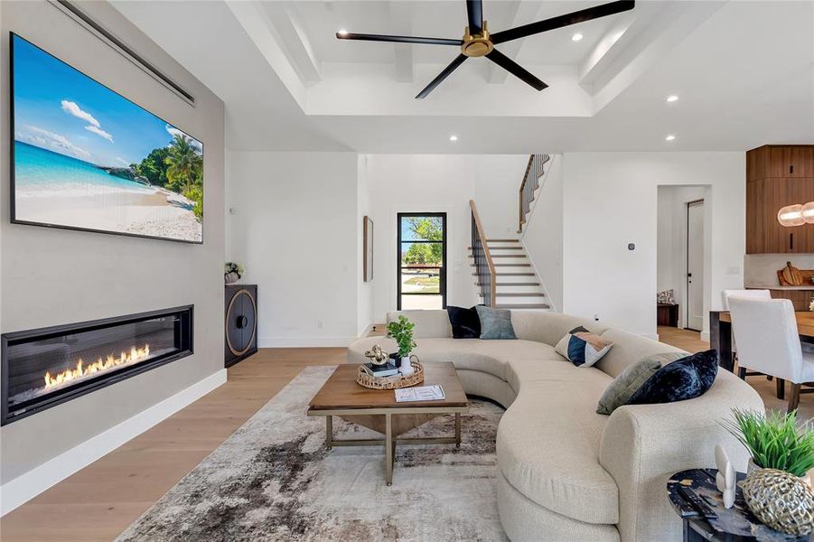 Living area featuring a tray ceiling, a glass covered fireplace, light wood-style flooring, recessed lighting, and stairway Living area featuring a tray ceiling, a glass covered fireplace, light wood-style flooring, recessed lighting, and stairway