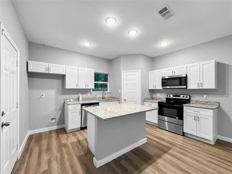 Kitchen with stainless steel appliances, white cabinetry, light wood-type flooring, a center island, and recessed lighting