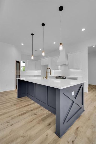 Kitchen featuring a large island with sink, hanging light fixtures, custom range hood, white cabinetry, and light hardwood / wood-style floors