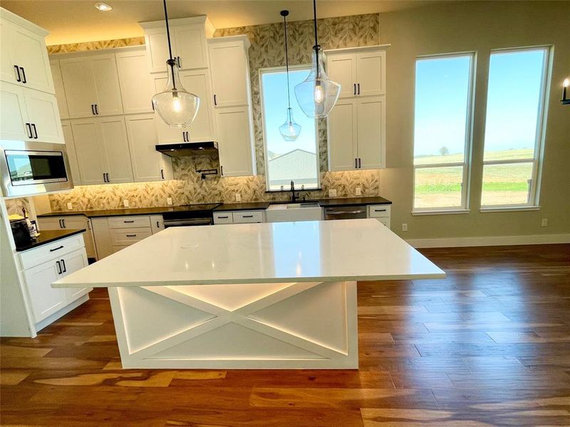Kitchen with white cabinetry, stainless steel microwave, dark wood-style floors, and decorative light fixtures