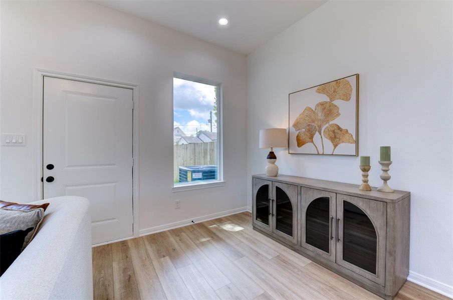 Living room sitting nook with floor-to-ceiling windows, hardwood floors, recessed lighting, and open backyard views with wood privacy fence.