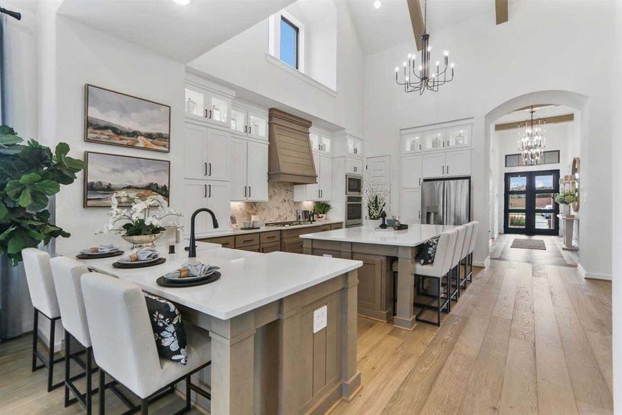 Kitchen with a spacious island, appliances with stainless steel finishes, white cabinetry, hanging light fixtures, and a breakfast bar area