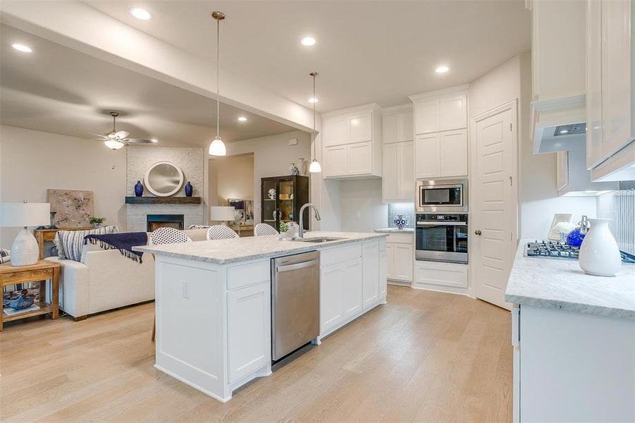 Kitchen featuring stainless steel appliances, white cabinetry, a center island with sink, and a fireplace