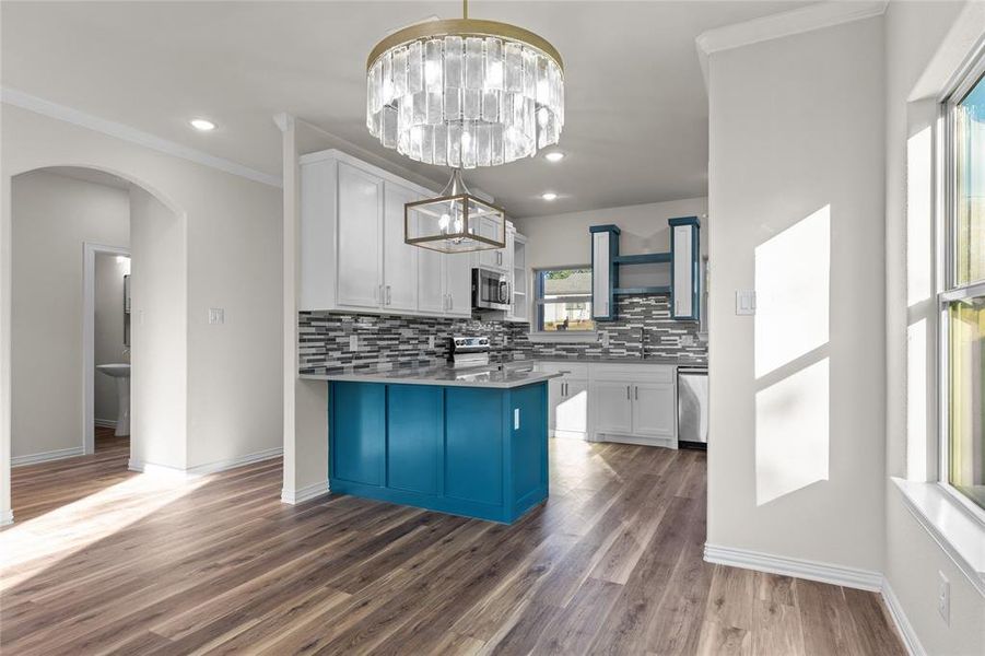 Kitchen featuring white cabinets, hanging light fixtures, backsplash, dark wood-style floors, and ornamental molding