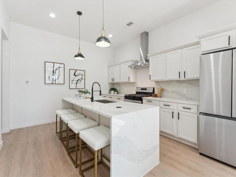 Kitchen featuring a sink, white cabinetry, appliances with stainless steel finishes, wall chimney exhaust hood, and a center island with sink