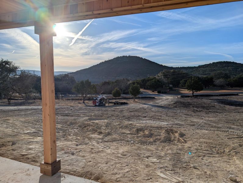 Expansive outdoor space featuring a raw land lot, distant hills, mature trees, and a wooden porch post with a visible concrete base