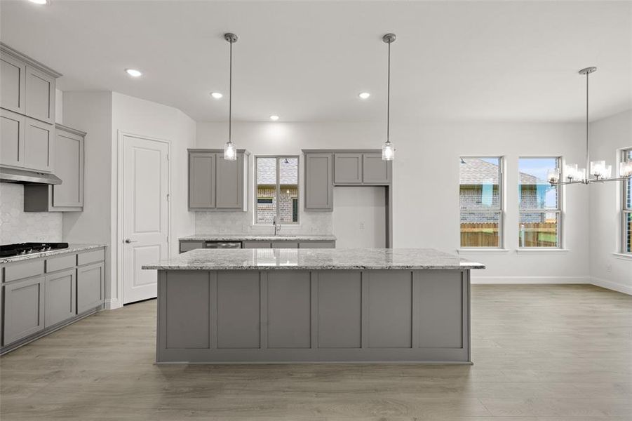 Kitchen with gray cabinets, tasteful backsplash, light wood-style flooring, a center island, and stainless steel gas cooktop Kitchen with gray cabinets, tasteful backsplash, light wood-style flooring, a center island, and stainless steel gas cooktop