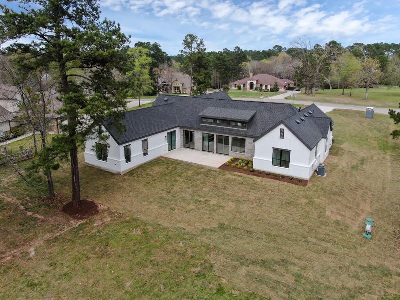 Rear aerial perspective highlighting the home’s architectural design, covered patio area, and the generous backyard space.