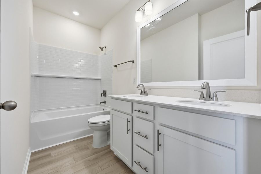 Full bath featuring shower / washtub combination, double vanity, and light wood-style flooring