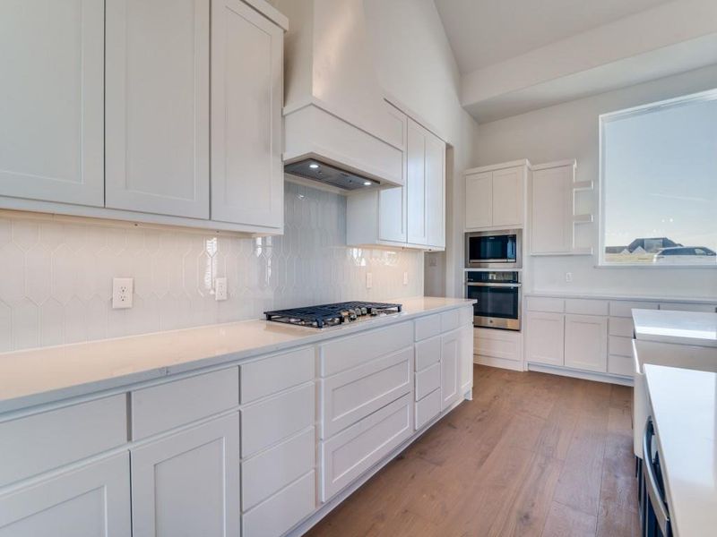 Kitchen featuring white cabinets, decorative backsplash, stainless steel appliances, light wood-type flooring, and open shelves
