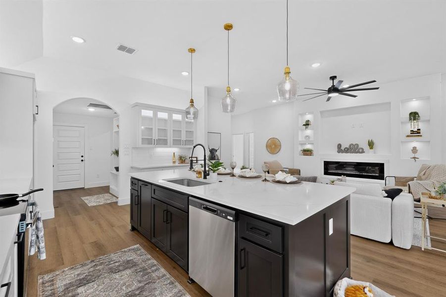 Central kitchen island with a white countertop, dark cabinetry, and integrated stainless steel dishwasher