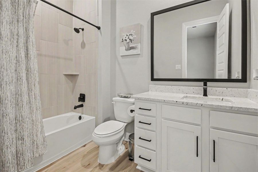 This bathroom features a modern design with a white vanity, black fixtures, and a large framed mirror. It includes a bathtub with a shower curtain, wood-style flooring, and a neutral color scheme, creating a clean and inviting space. This bathroom features a modern design with a white vanity, black fixtures, and a large framed mirror. It includes a bathtub with a shower curtain, wood-style flooring, and a neutral color scheme, creating a clean and inviting space.
