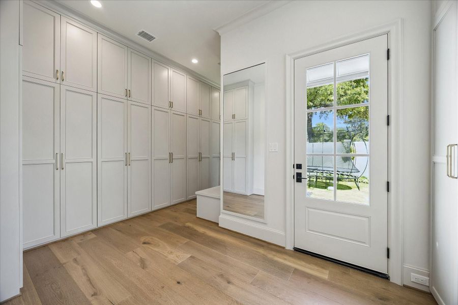 The primary closet features wall of extensive custom-built cabinetry with integrated hanging, shelving and storage space. Beautiful  French white oak wide plank flooring continues throughout, while a full-length mirror and direct exterior access to the side yard add convenience and a refined finishing touch.