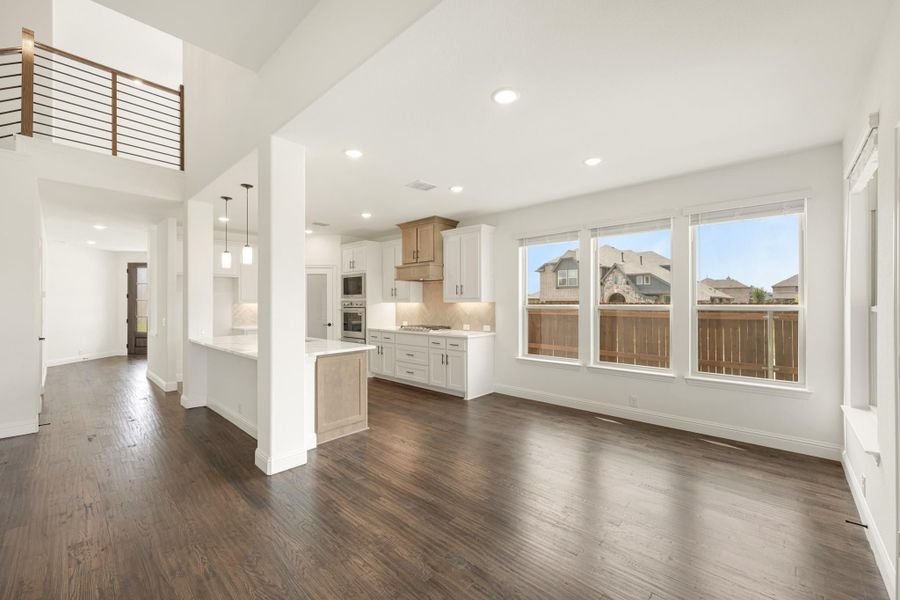 Open-concept living area with dark hardwood floors, white kitchen cabinets, center island, and second-floor balcony overlook