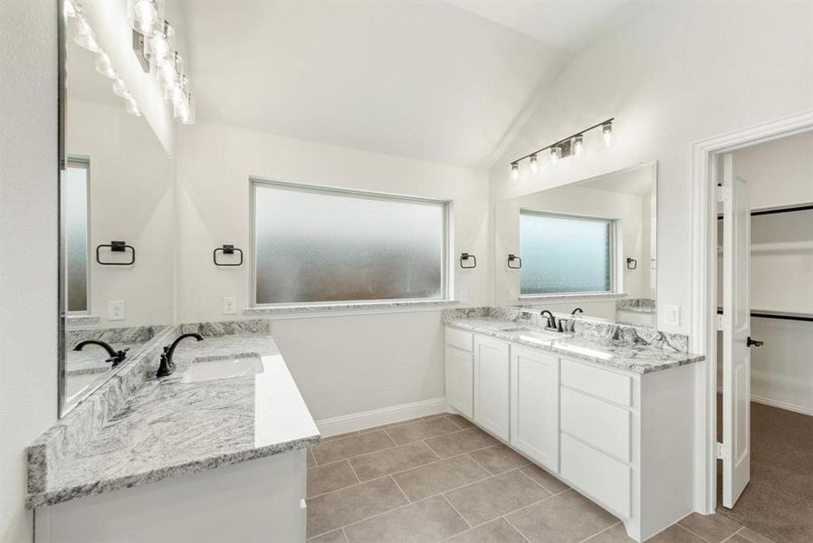 Bright bathroom featuring dual vanity with stone countertops, white cabinetry, dark bronze fixtures, and rectangular tile flooring Bright bathroom featuring dual vanity with stone countertops, white cabinetry, dark bronze fixtures, and rectangular tile flooring