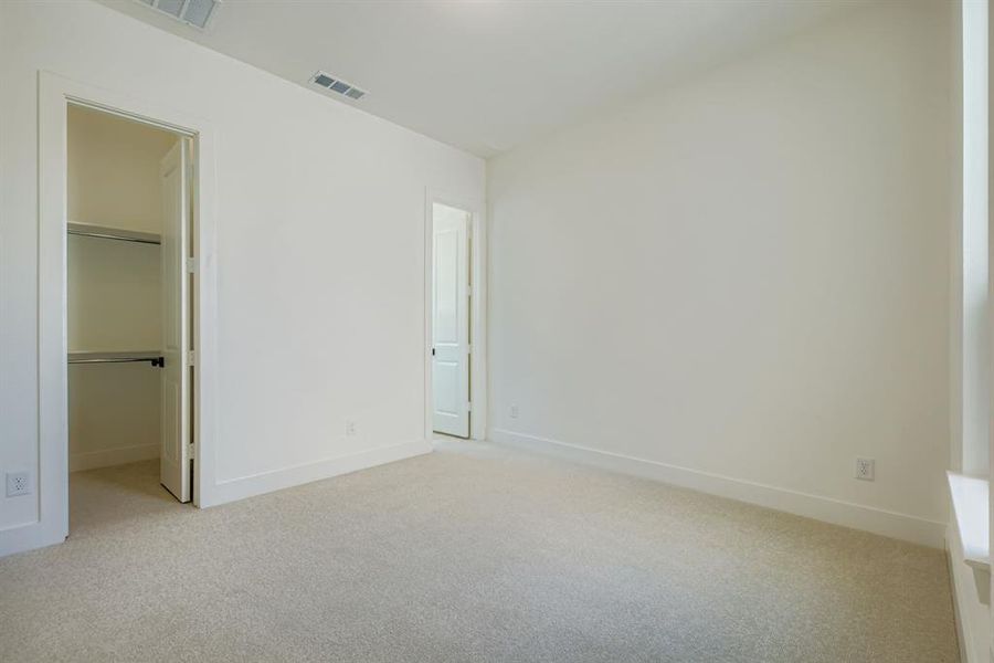 Unfurnished bedroom featuring light carpet and a spacious closet Unfurnished bedroom featuring light carpet and a spacious closet