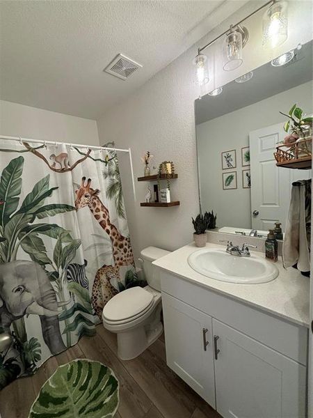 Full bathroom featuring dark wood-style floors, vanity, a textured ceiling, curtained shower, and a textured wall