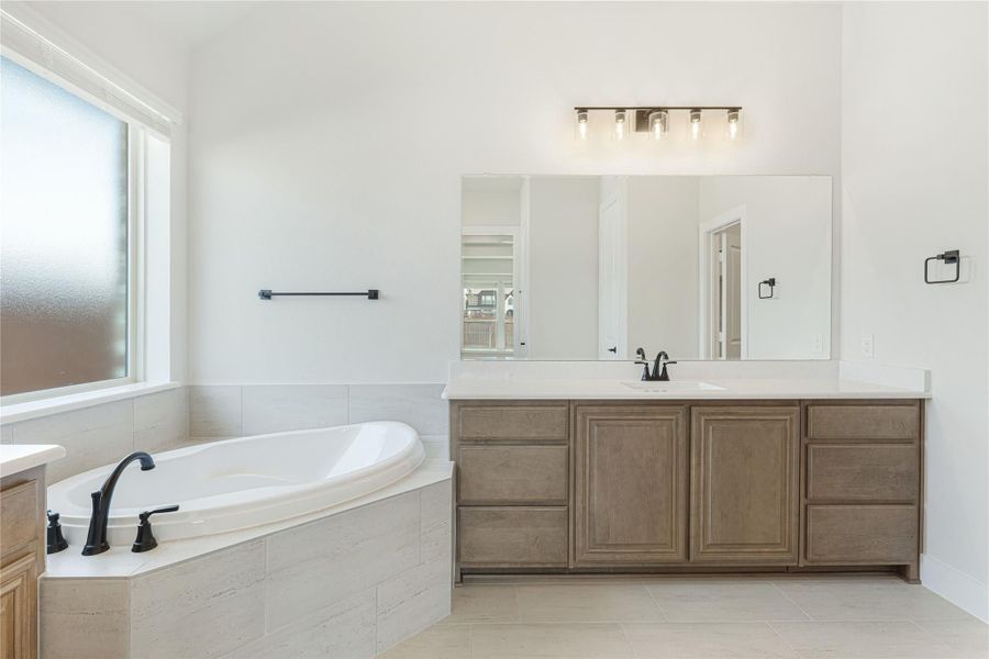 Master bathroom with corner soaking tub, wood vanity, white countertop, and large mirror with wall lighting. Master bathroom with corner soaking tub, wood vanity, white countertop, and large mirror with wall lighting.