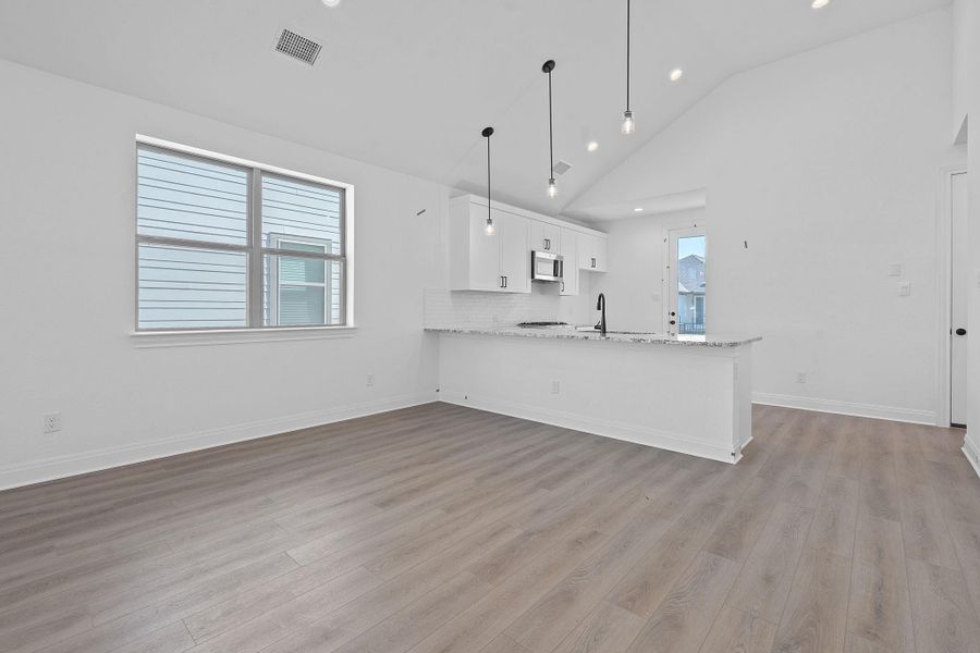 Kitchen with decorative backsplash, light stone countertops, white cabinetry, light wood-style floors, and a peninsula Kitchen with decorative backsplash, light stone countertops, white cabinetry, light wood-style floors, and a peninsula